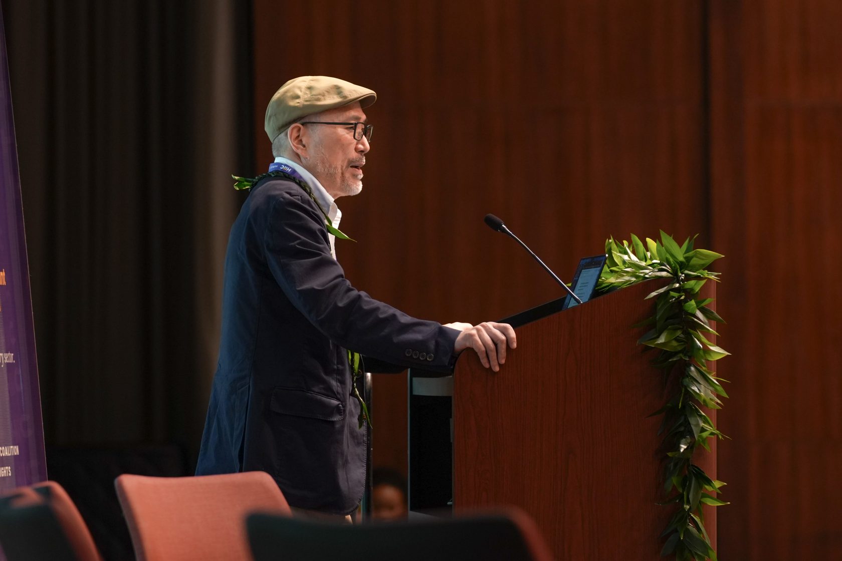 Scot Nakagawa speaking from the lei-draped podium in the Keoni Auditorium